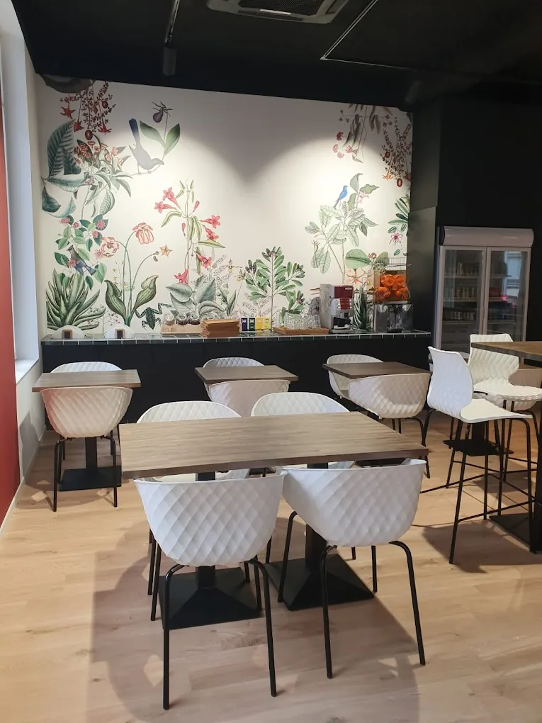 La salle : papier peint fleuri, tables en bois et chaises blanches